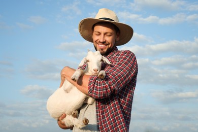 Photo of Farmer with cute goatling outdoors. Baby animal