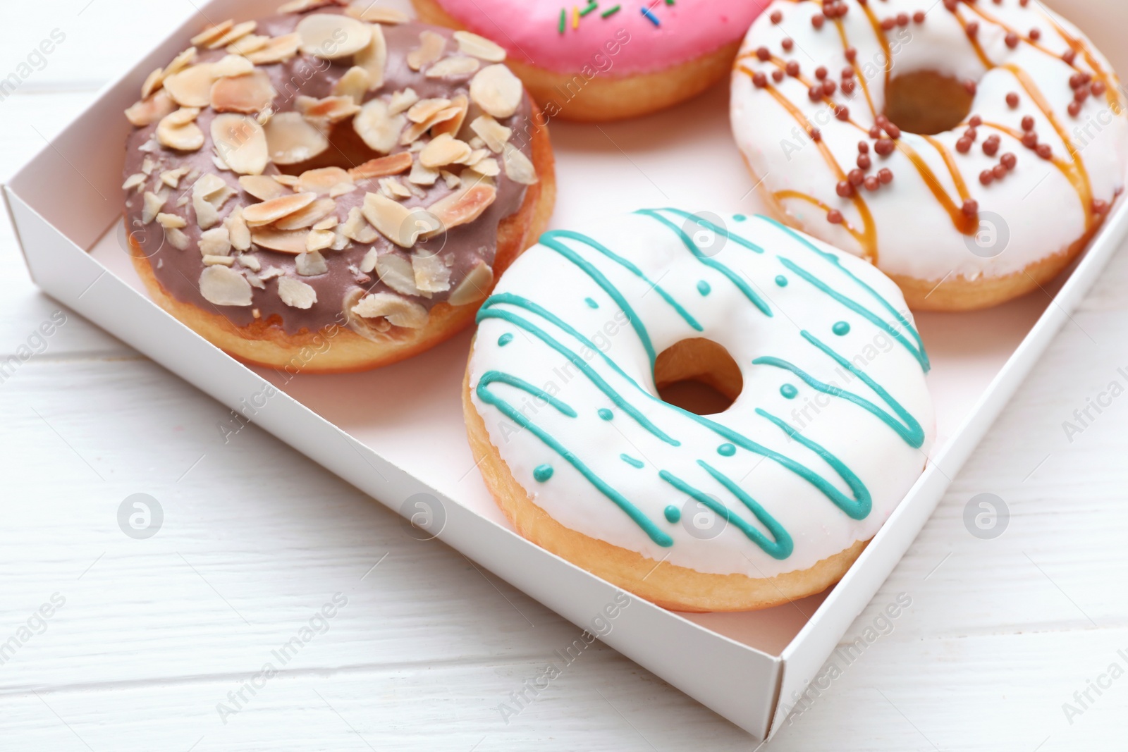 Photo of Box with different tasty glazed donuts on white wooden table, closeup