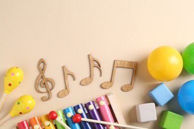 Photo of Baby song concept. Wooden notes, kids xylophone and toys on beige background, flat lay. Space for text