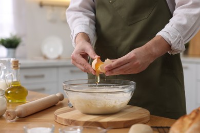 Photo of Making bread. Man putting raw egg into dough at wooden table in kitchen, closeup