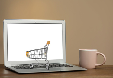 Image of Online shopping. Laptop with small cart and cup on table