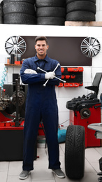 Photo of Professional worker with wheel and wrench in shop of modern tire service