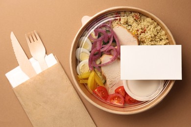 Photo of Tasty food in container with wooden fork and knife on beige background, flat lay. Space for text