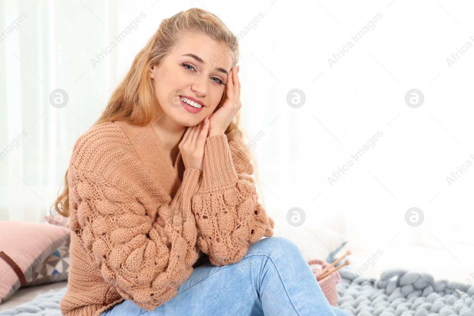Photo of Attractive young woman in cozy warm sweater sitting on floor at home. Space for text