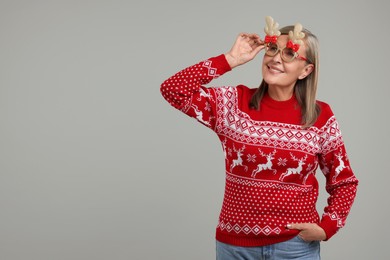 Happy senior woman in Christmas sweater and funny glasses on grey background. Space for text