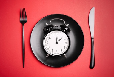 Photo of Alarm clock, plate and cutlery on red background, flat lay. Diet regime