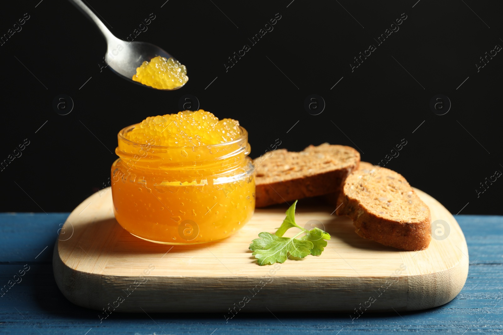 Photo of Taking fresh pike caviar from glass jar on blue wooden table, closeup