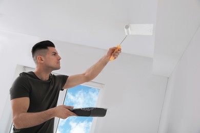 Man painting ceiling with roller in room