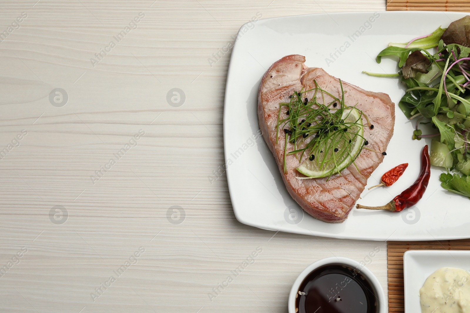 Photo of Delicious tuna steak served with salad and sauces on white wooden table, flat lay. Space for text