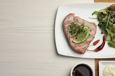 Delicious tuna steak served with salad and sauces on white wooden table, flat lay. Space for text