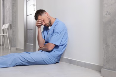 Exhausted doctor sitting near grey wall in hospital corridor