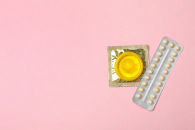 Photo of Condoms and birth control pills on pink background, top view with space for text. Safe sex