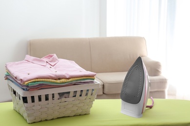 Board with modern iron and laundry basket at home