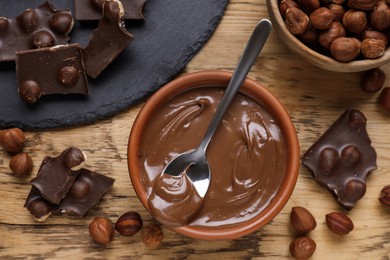 Chocolate pieces, bowl of sweet paste and nuts on wooden table, flat lay
