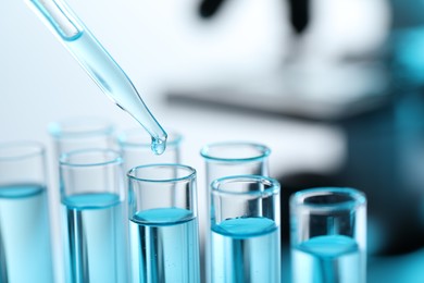 Photo of Dripping liquid from pipette into test tube on blurred background, closeup