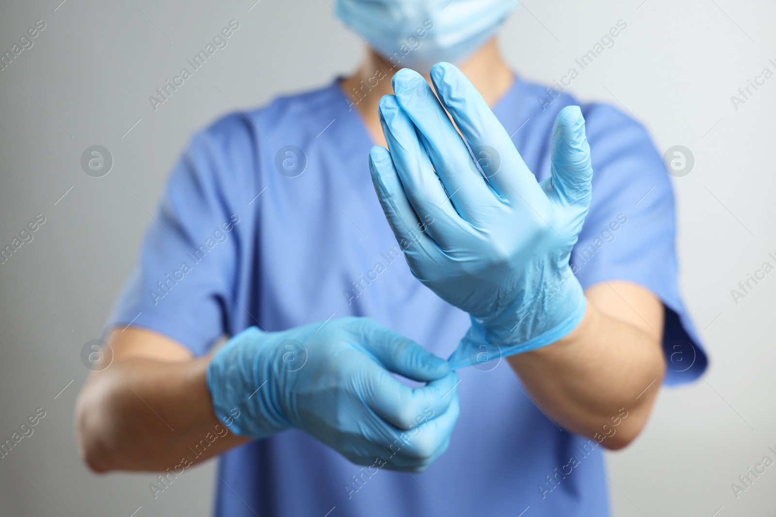 Photo of Doctor wearing light blue medical gloves on grey background, closeup