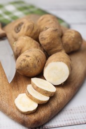 Photo of Whole and cut turnip rooted chervil tubers on light wooden table, closeup