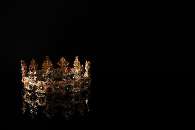 Photo of Beautiful golden crown with gems on dark mirror surface. Space for text
