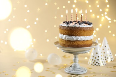 Photo of Tasty cake with burning candles on beige background against blurred lights. Space for text