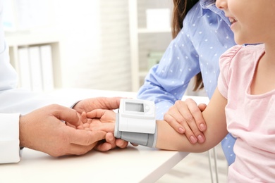 Doctor checking little girl's pulse with medical device in hospital, closeup