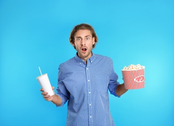 Emotional man with popcorn and beverage during cinema show on color background