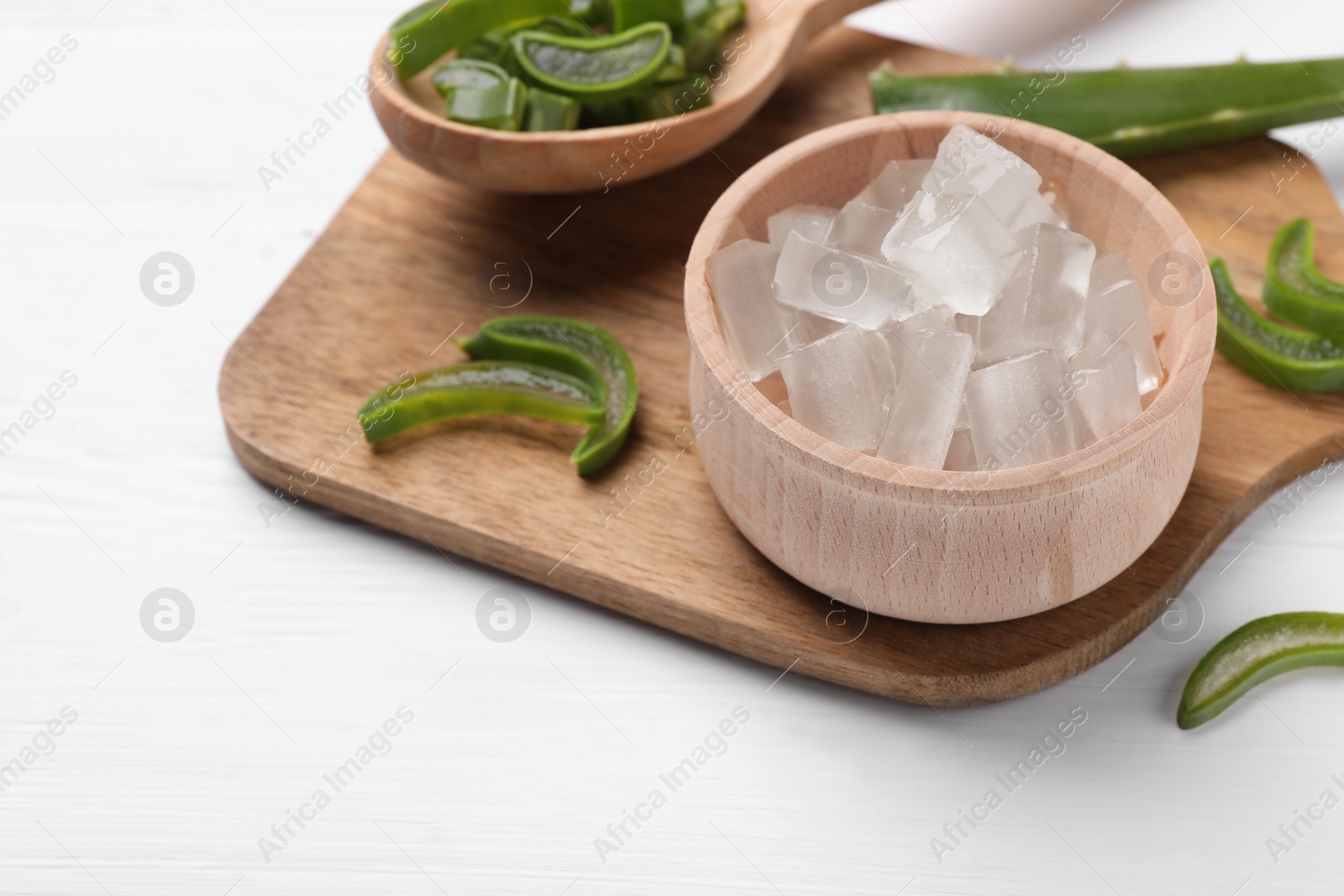 Photo of Aloe vera gel and slices of plant on white wooden table, closeup. Space for text