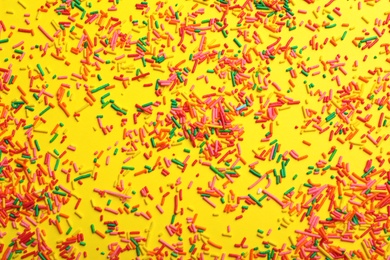 Photo of Bright colorful sprinkles on yellow background, flat lay. Confectionery decor