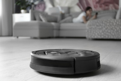 Photo of Modern robotic vacuum cleaner and blurred woman resting on background