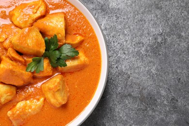 Bowl of delicious chicken curry on grey table, top view. Space for text