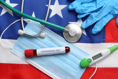 Photo of Test tube with blood, protective mask, gloves, stethoscope and thermometer on American flag, flat lay. Coronavirus pandemic in USA