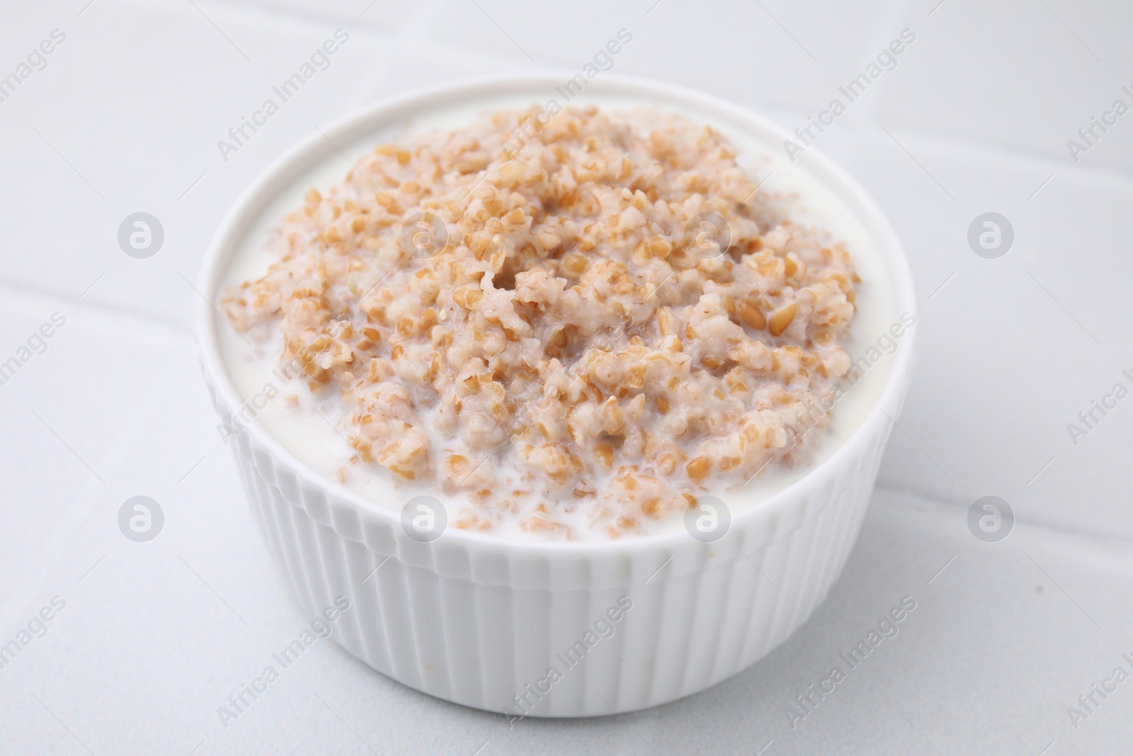 Photo of Tasty wheat porridge with milk in bowl on white table, closeup