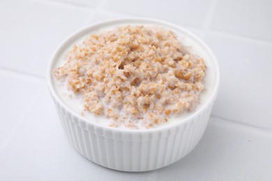 Photo of Tasty wheat porridge with milk in bowl on white table, closeup