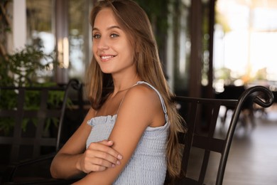 Beautiful young woman sitting on indoor terrace in cafe, space for text