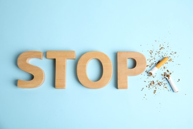 Photo of Broken cigarette near word Stop made with wooden letters on light blue background, flat lay. Quitting smoking concept