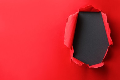 Photo of Hole in red paper on black background, space for text