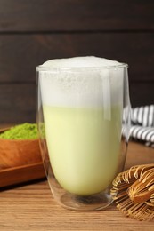 Glass of tasty matcha latte and bamboo whisk on wooden table