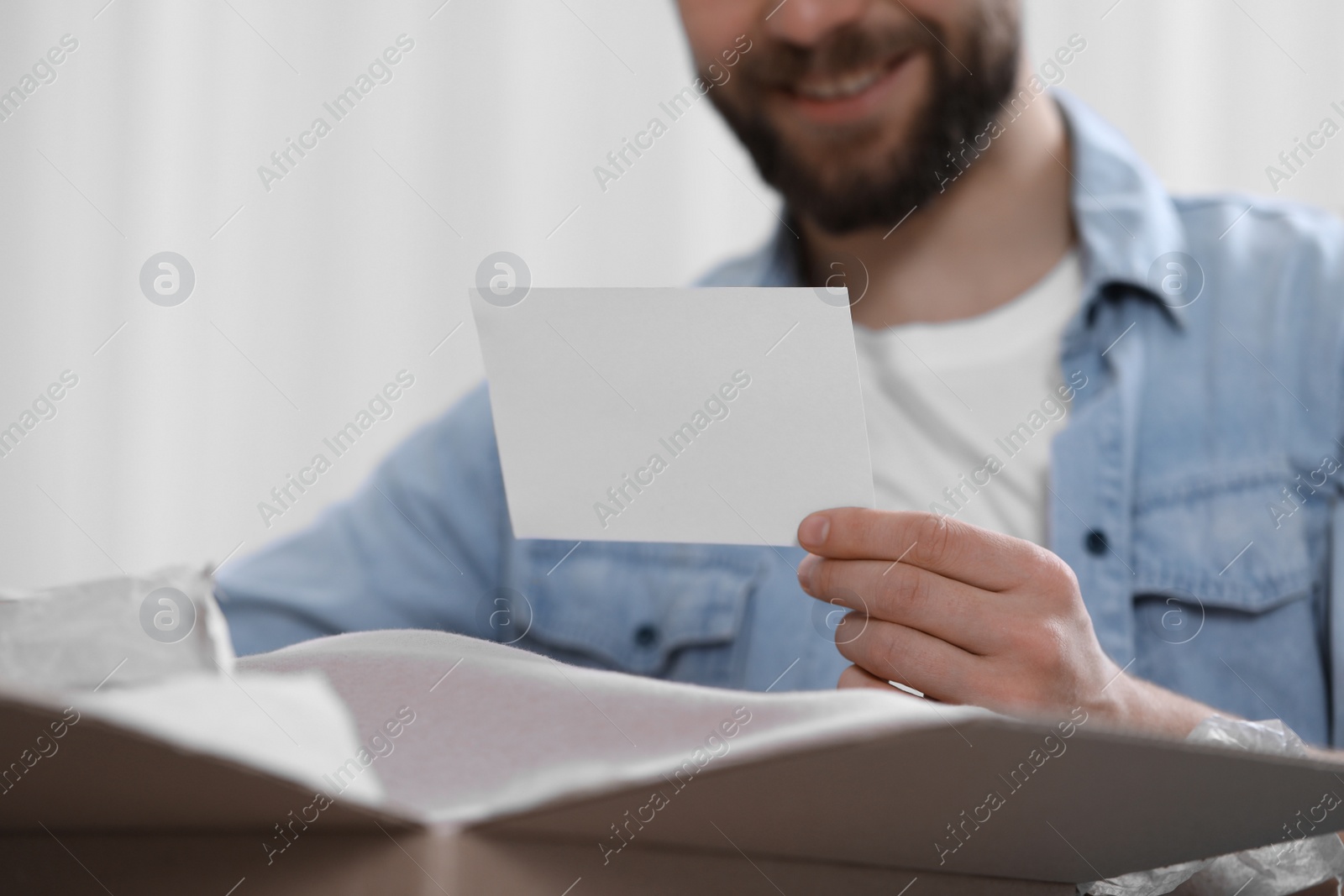 Photo of Man holding greeting card near parcel with Christmas gift, closeup