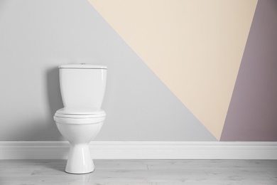 Photo of New toilet bowl near color wall indoors. Space for text