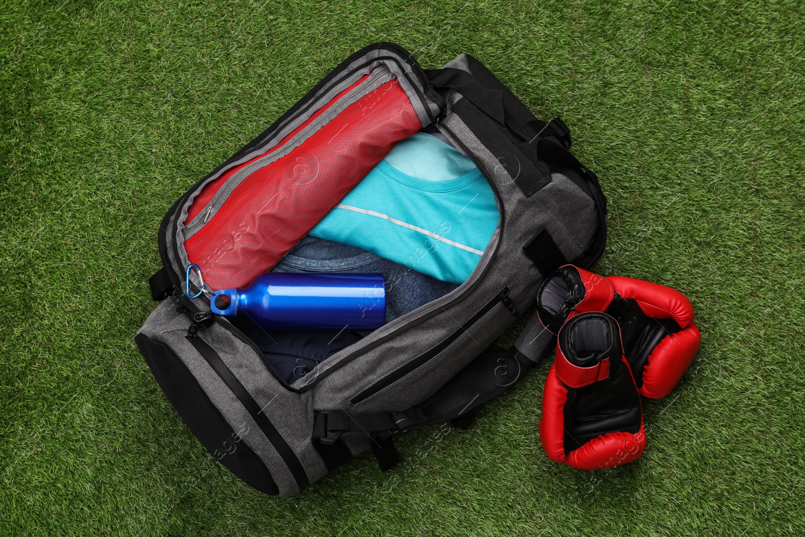Photo of Gym bag and sports equipment on green grass, flat lay