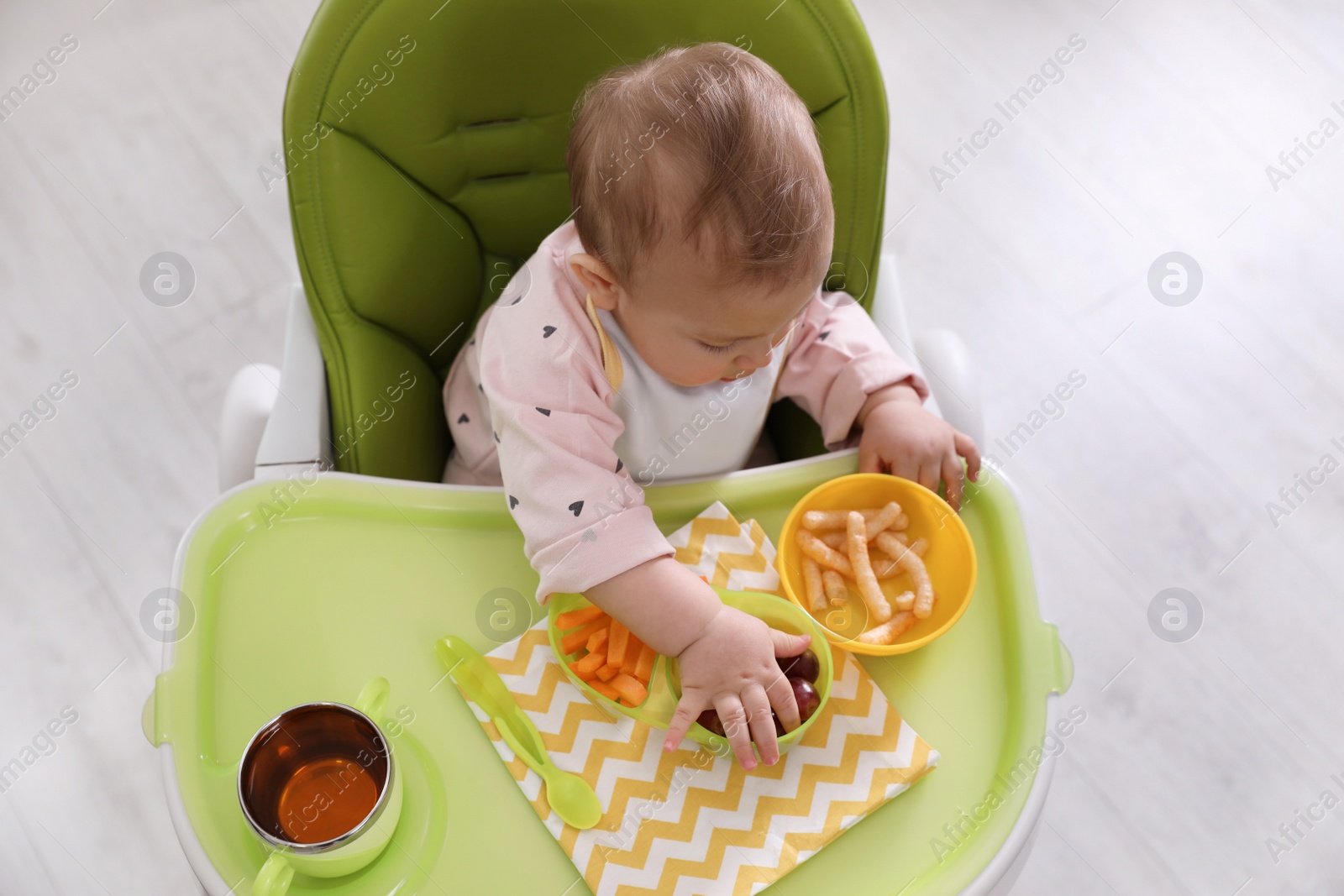 Photo of Cute little baby eating food in high chair indoors, top view