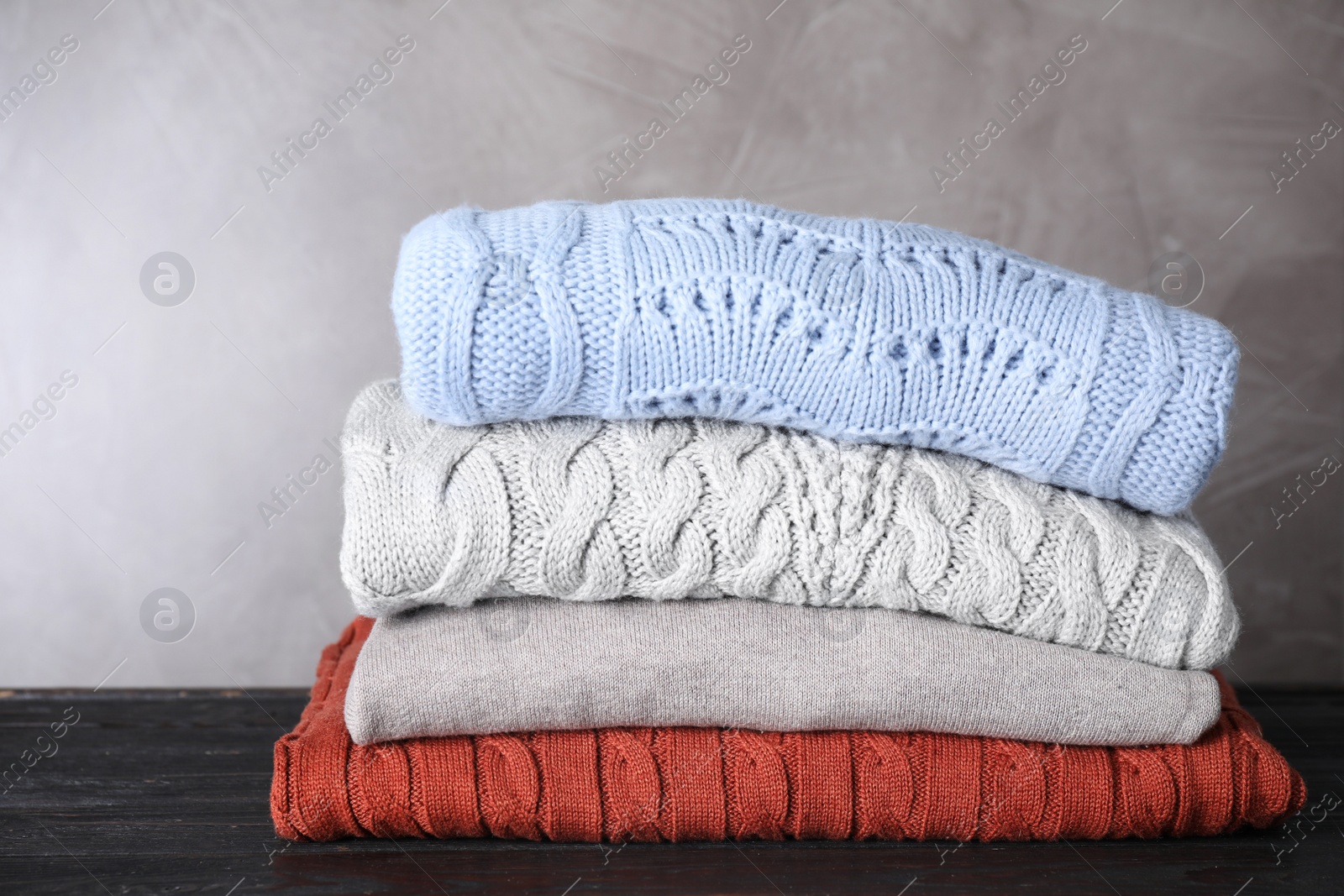 Image of Stack of folded warm sweaters on black wooden table 