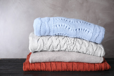 Stack of folded warm sweaters on black wooden table 