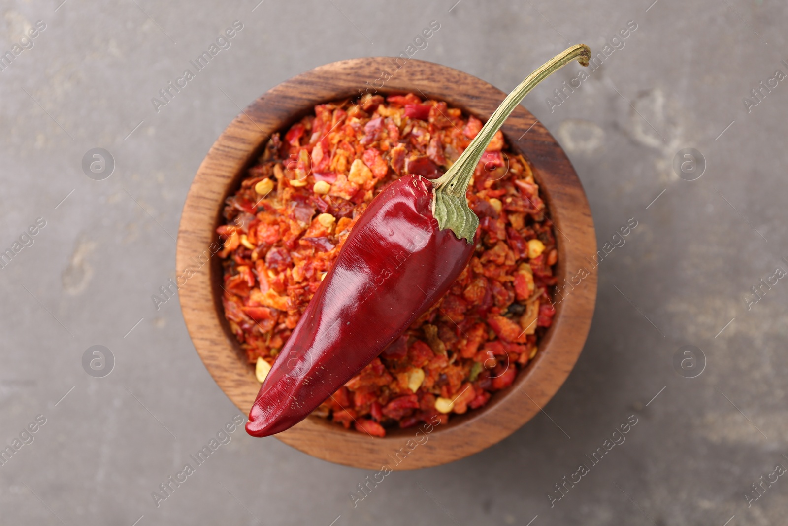 Photo of Chili pepper flakes in bowl and pod on grey table, top view