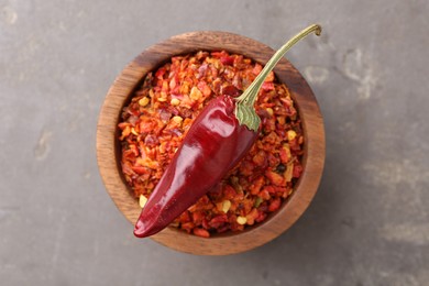 Photo of Chili pepper flakes in bowl and pod on grey table, top view