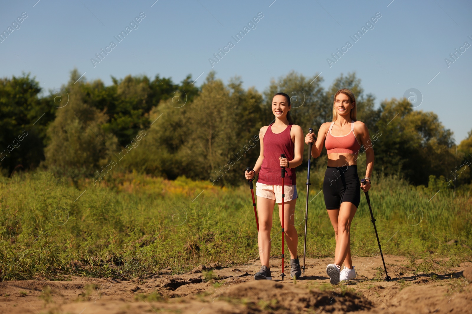 Photo of Happy women practicing Nordic walking with poles outdoors on sunny day