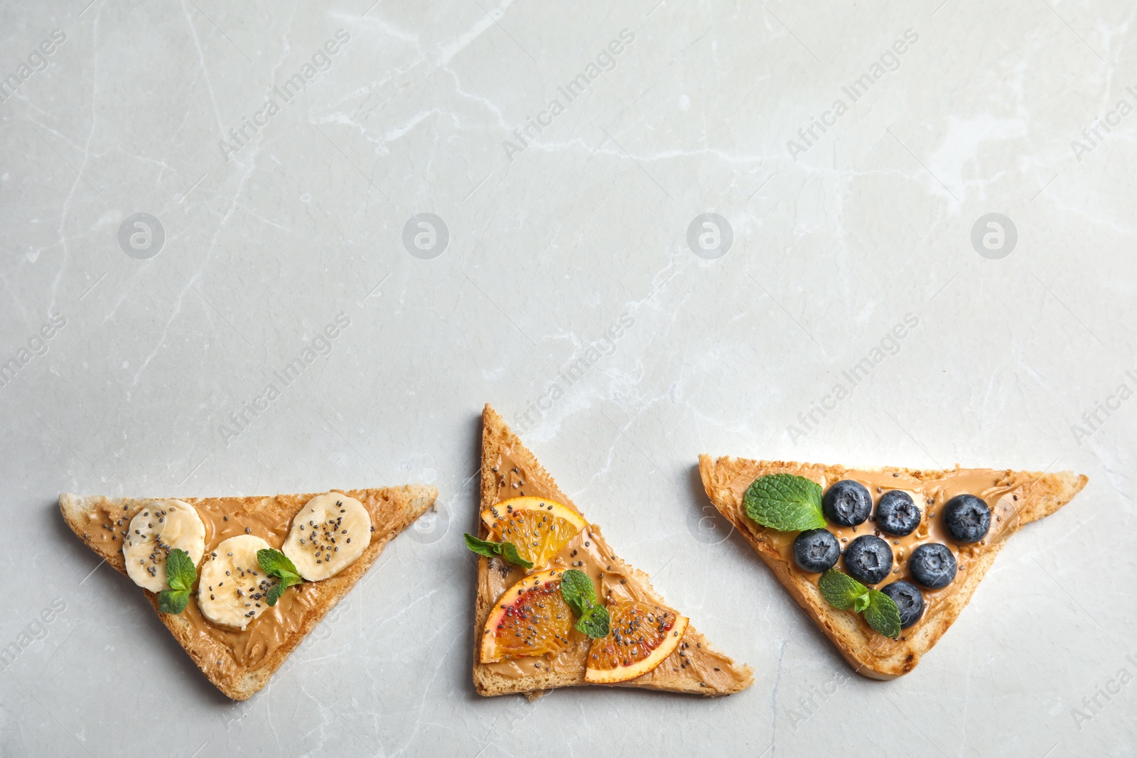 Photo of Different toasts with fruits, blueberries, peanut butter and chia seeds on grey background, top view. Space for text