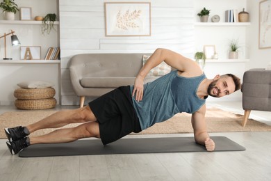 Photo of Handsome man doing side plank exercise on yoga mat at home