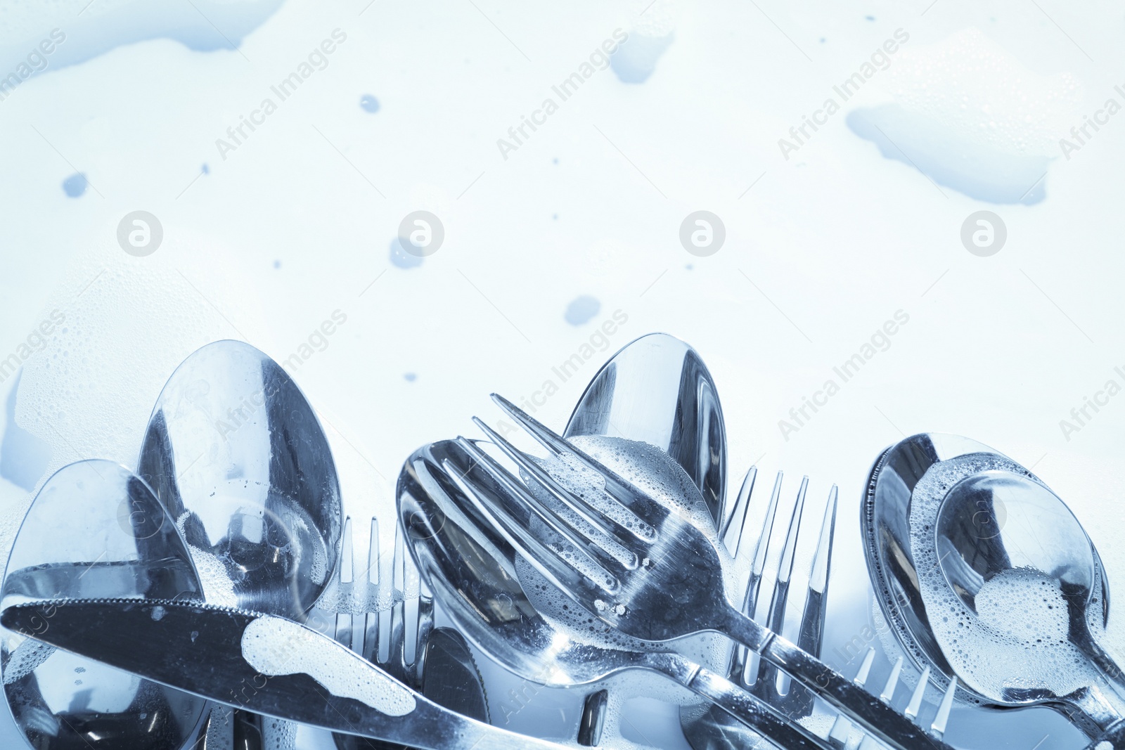 Photo of Different silverware in foam, flat lay with space for text. Toned in blue