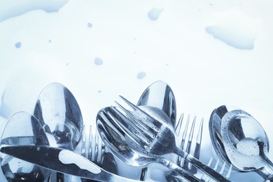 Photo of Different silverware in foam, flat lay with space for text. Toned in blue