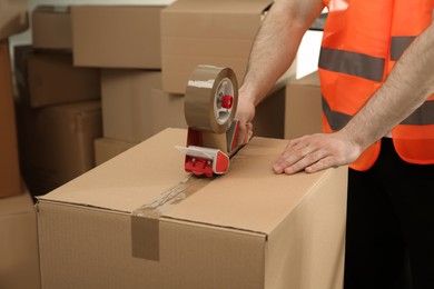 Worker taping cardboard box indoors, closeup view